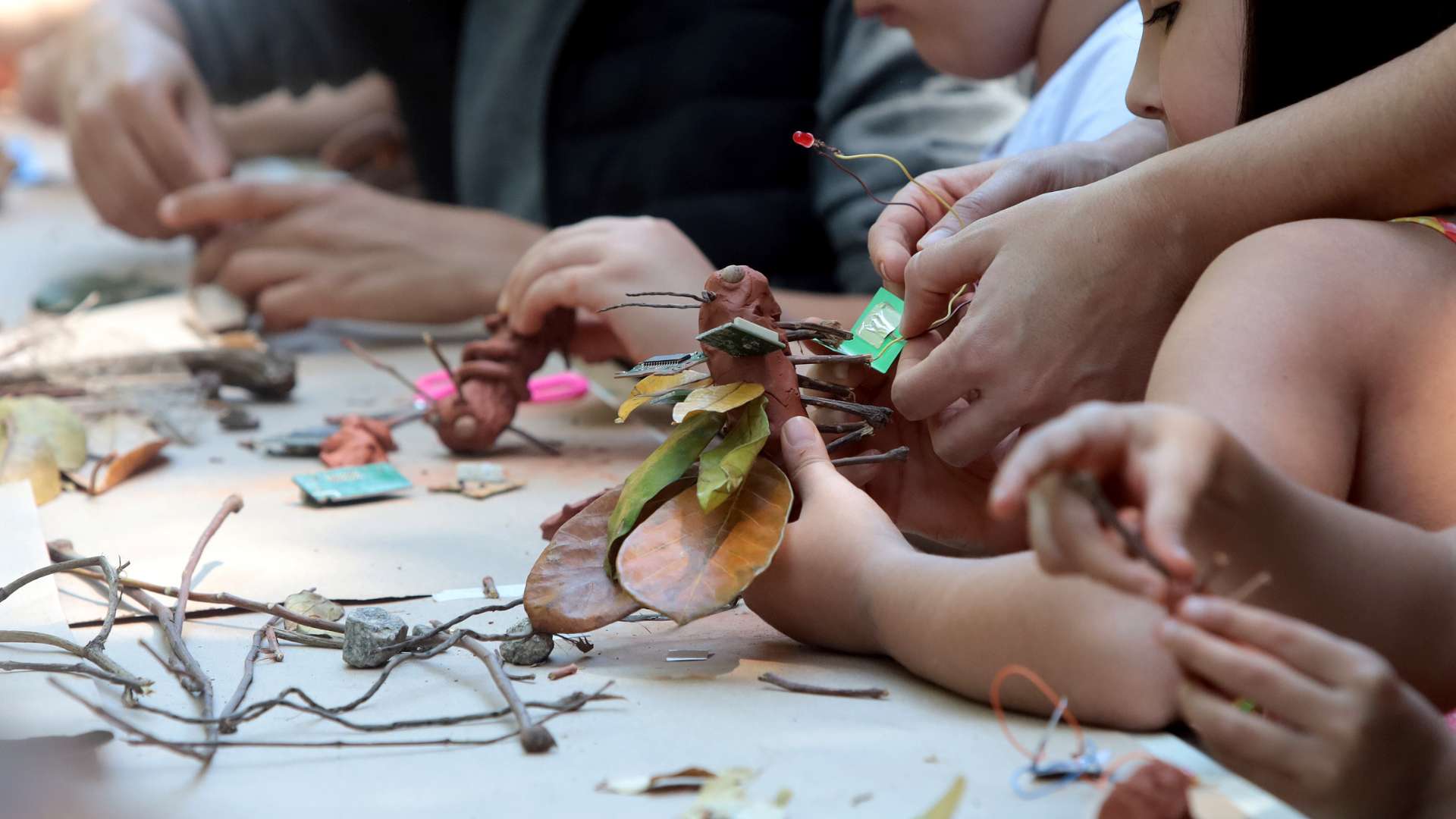 Crianças e adultos criando juntos com materiais naturais e eletrônicos em oficina do pequenoLab — folhas, galhos, argila e circuitos